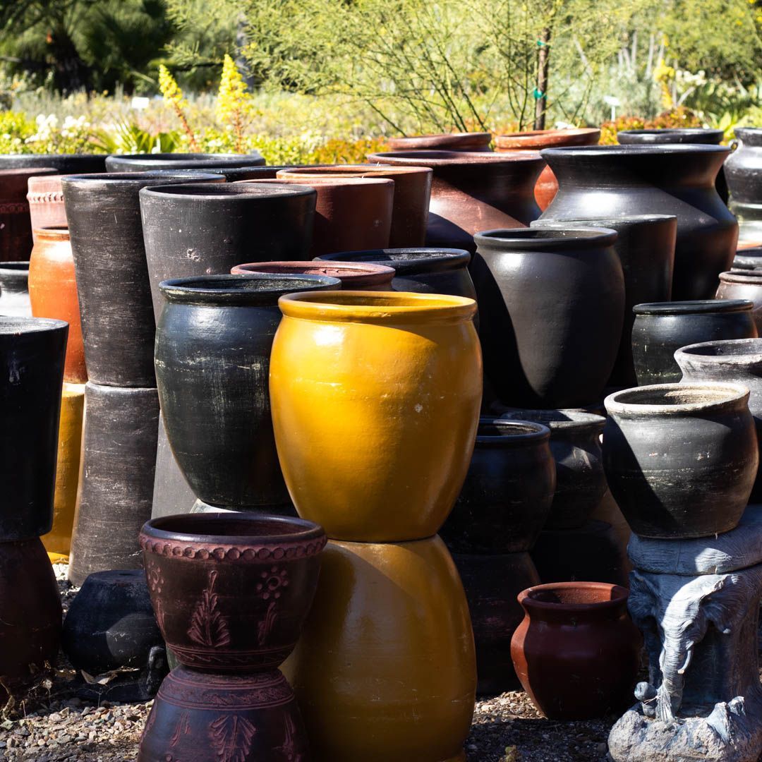Various ceramic pots in shades of black, brown, and yellow, stacked in an outdoor setting.