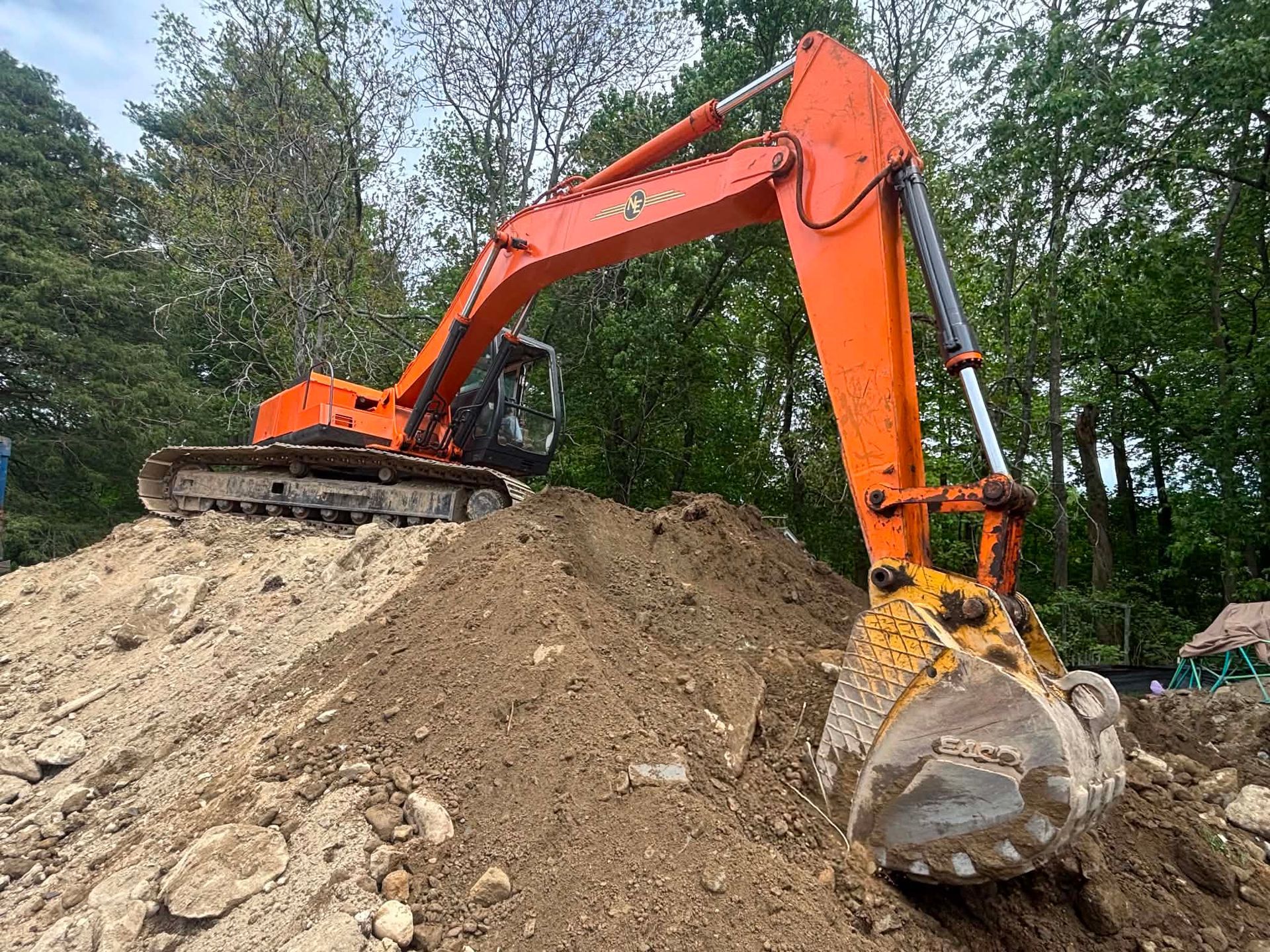 Orange excavator digging a dirt mound at a wooded construction site