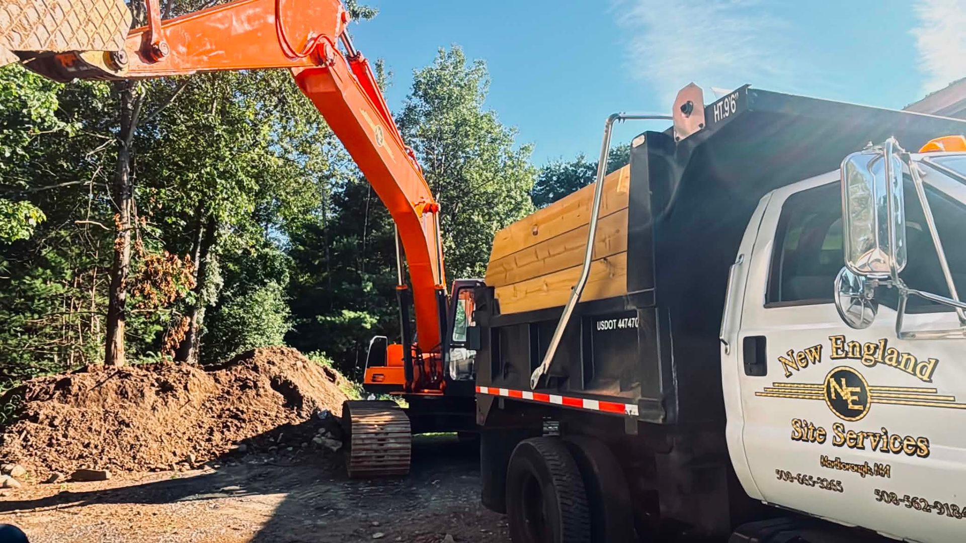 Orange excavator loading dirt into a dump truck at a wooded construction site