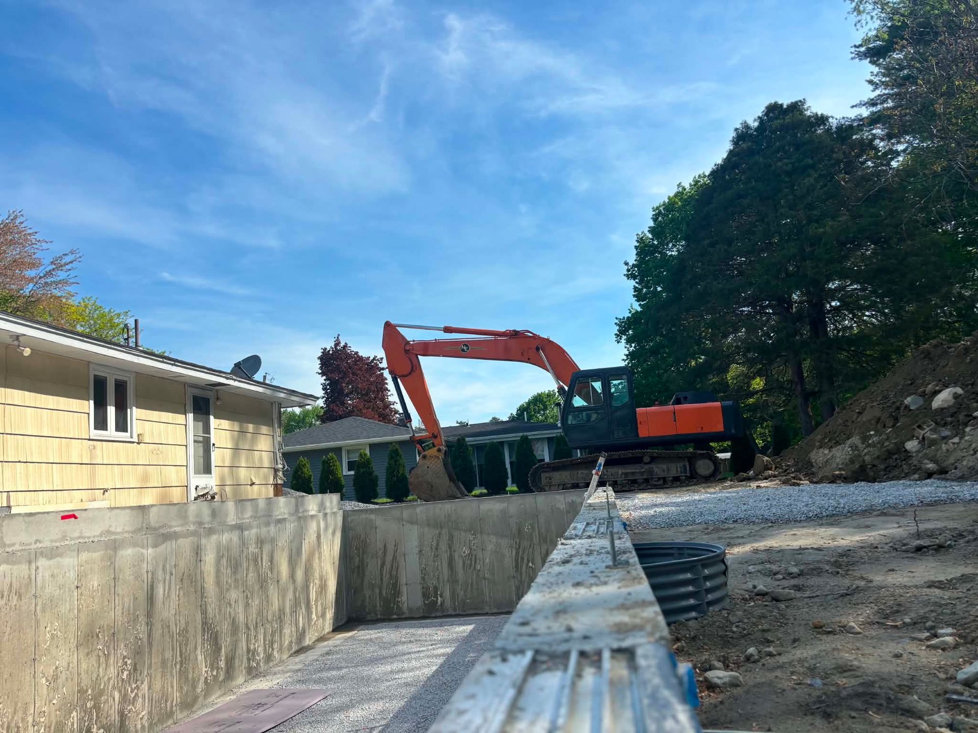 Construction excavator beside a concrete retaining wall at a roadside site under a blue sky