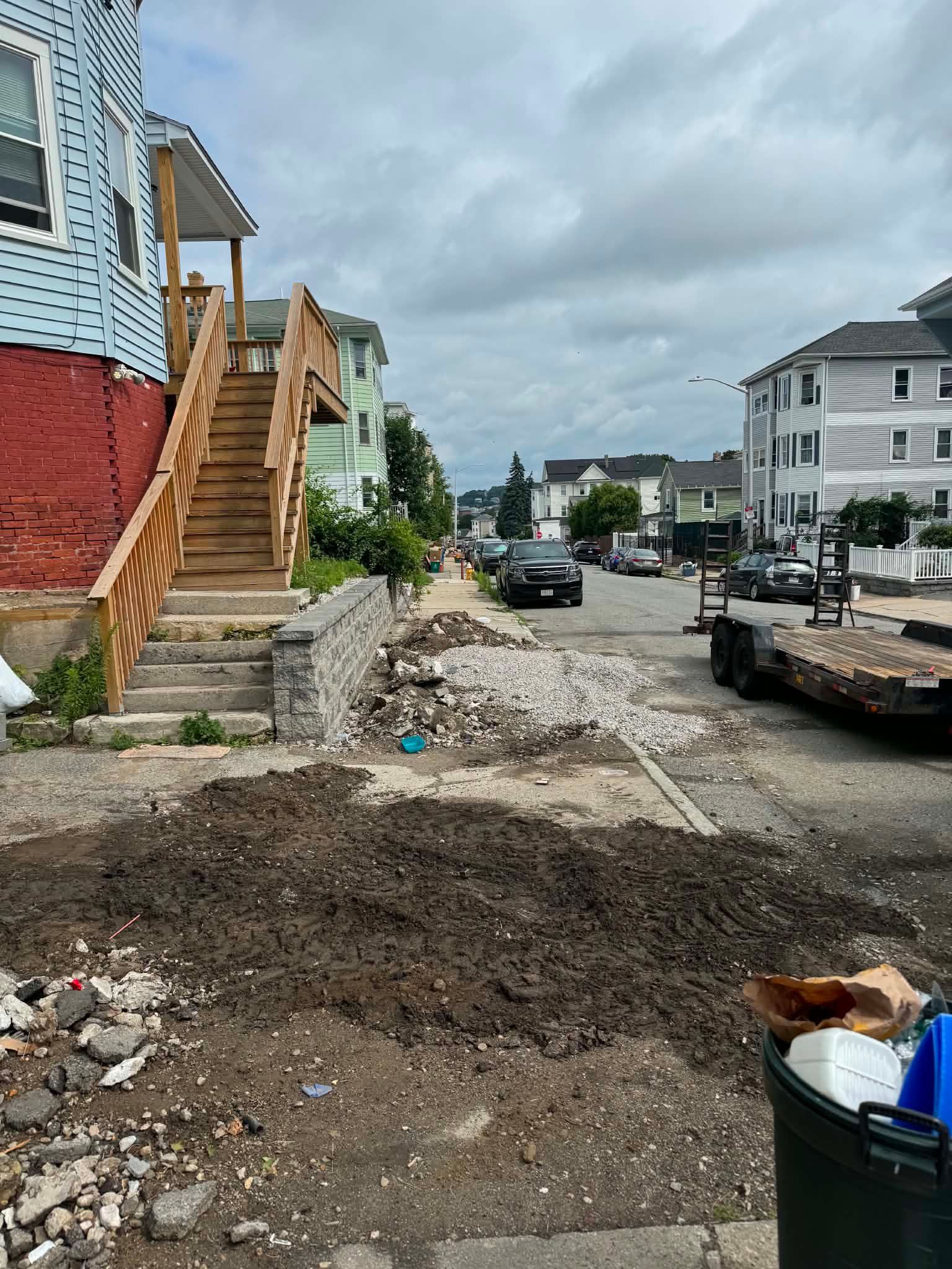 Damaged residential street with broken pavement, debris, parked truck, and cloudy sky