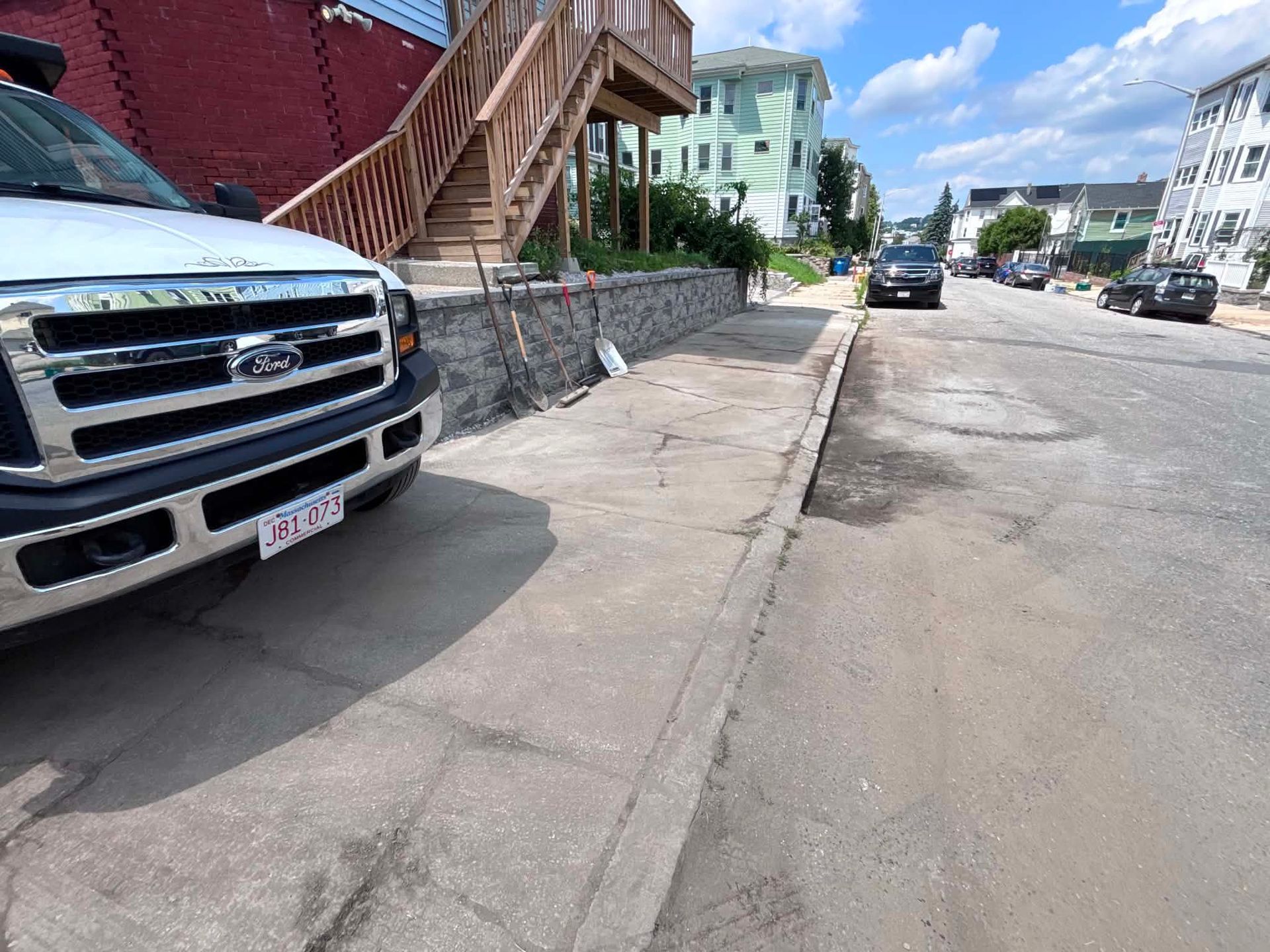 Sunny residential street with parked pickup truck, sidewalk, and row houses along the curb