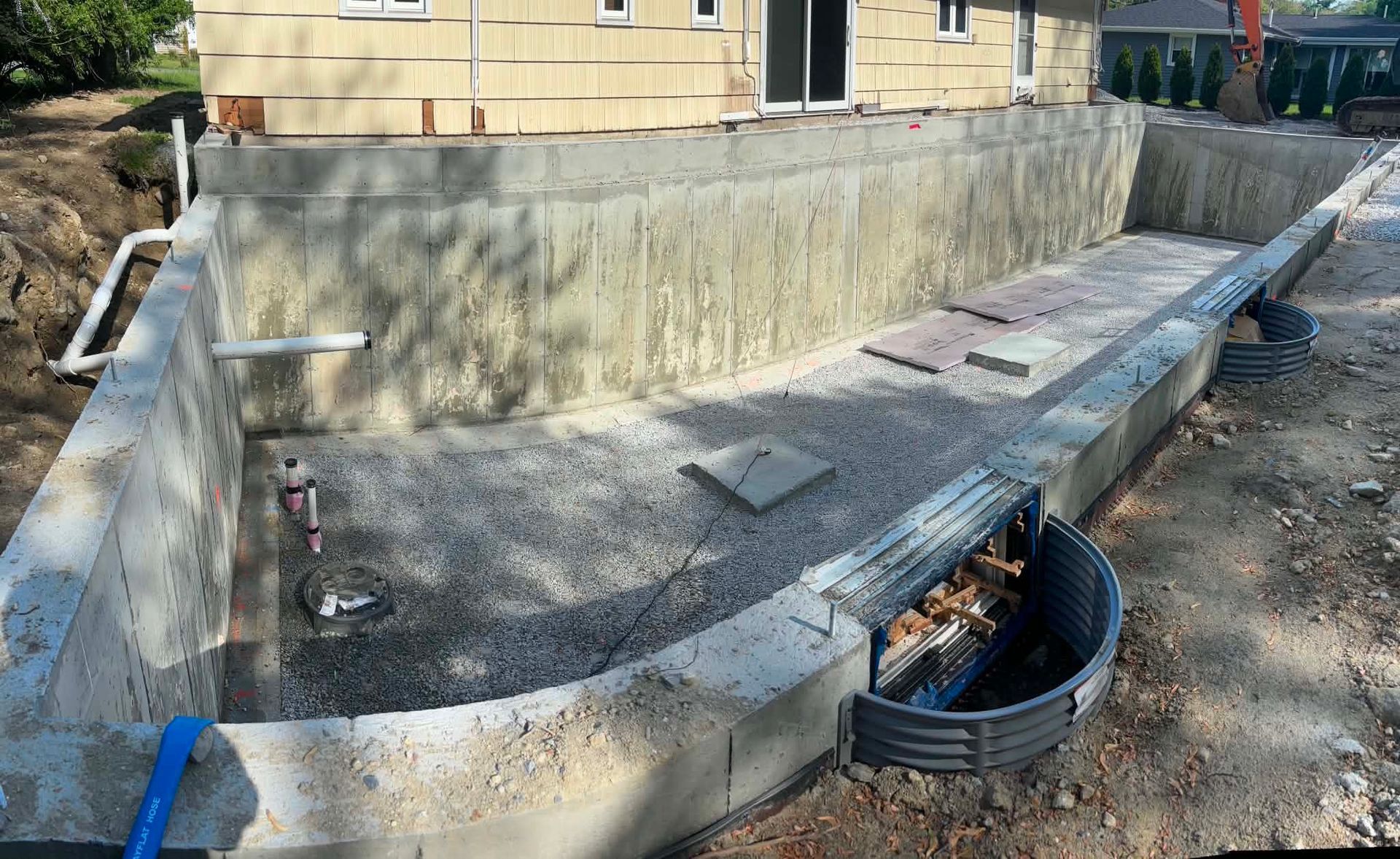 Concrete retaining wall and curved walkway under construction beside a house, with drainage grate and steps.