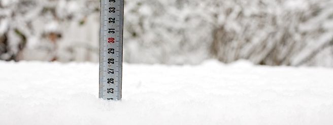 A measuring tool is standing in the middle of a pile of snow.