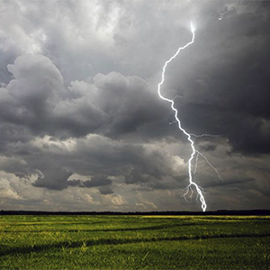 Lightning strikes a green field under a cloudy, gray sky.