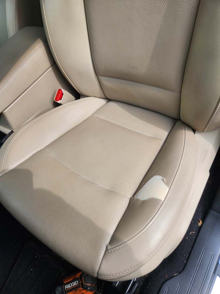 Beige leather car seat with a torn area.