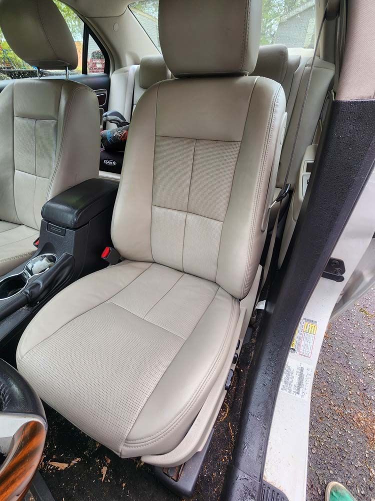Tan leather car seat with central console and steering wheel visible.