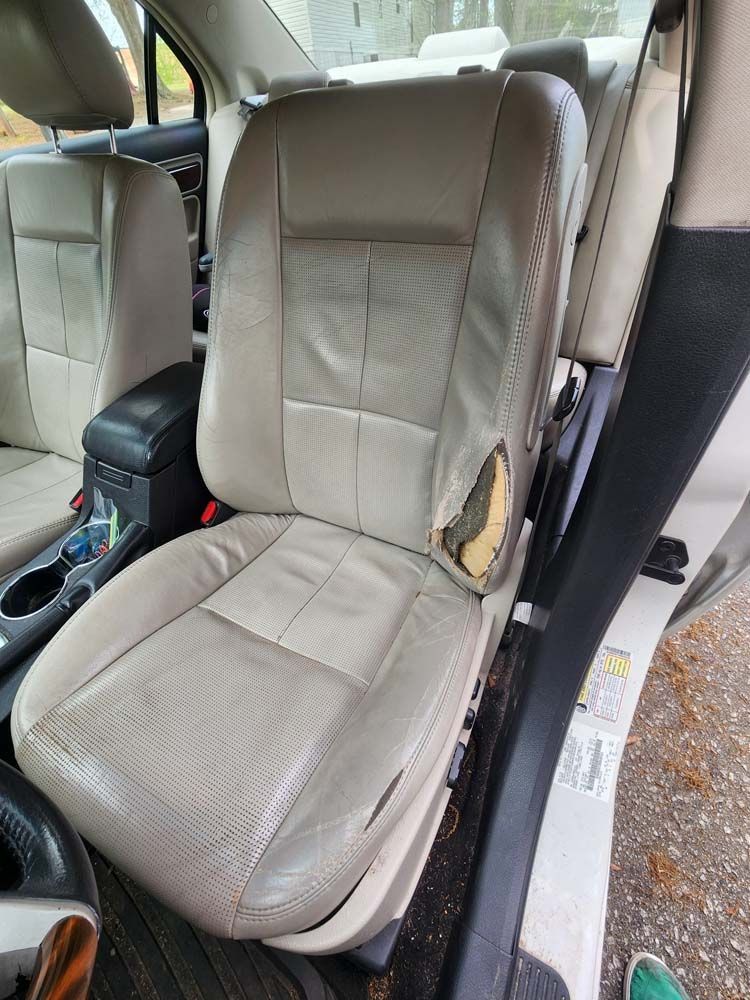 Beige car seat with ripped leather; interior car view.