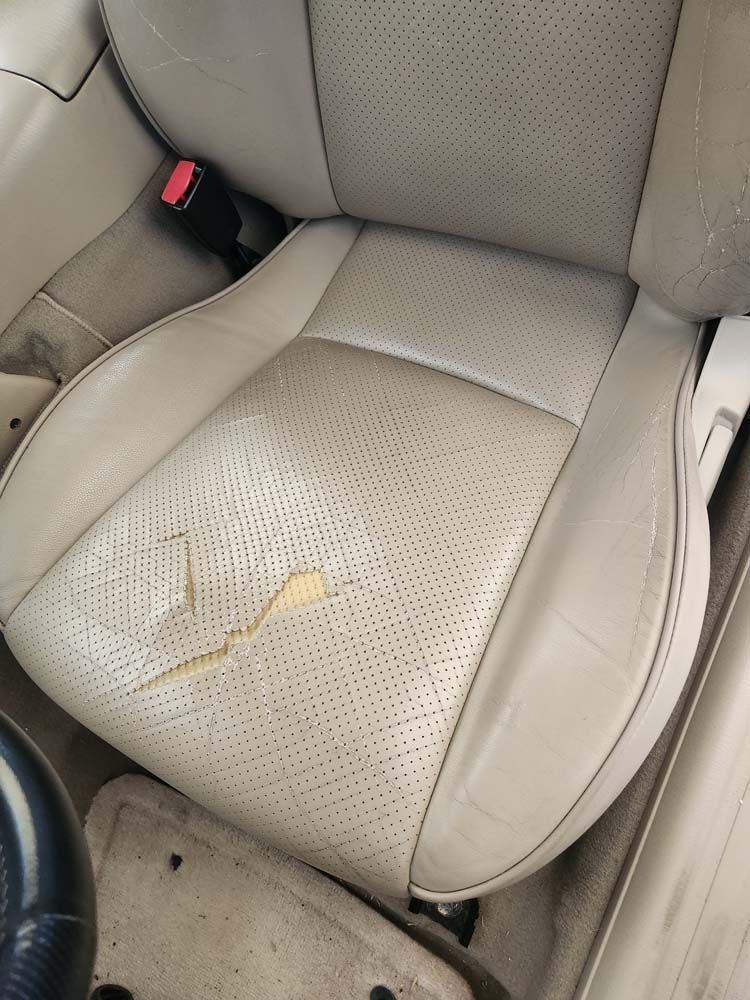 Beige car seat with ripped leather in the seat area, visible perforations.
