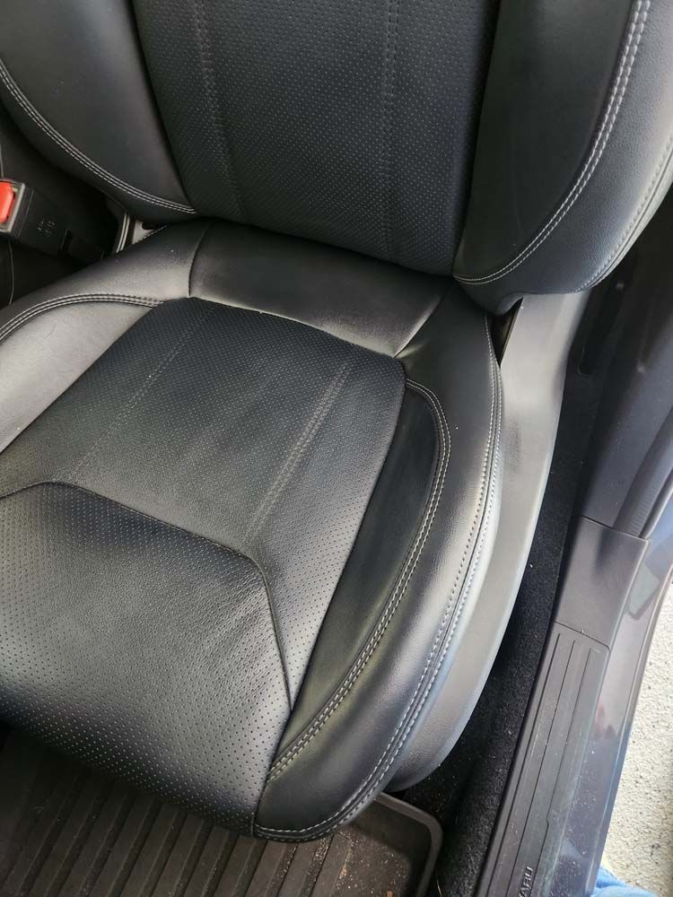 Black leather car seat with perforated seat cushion and stitching detail.