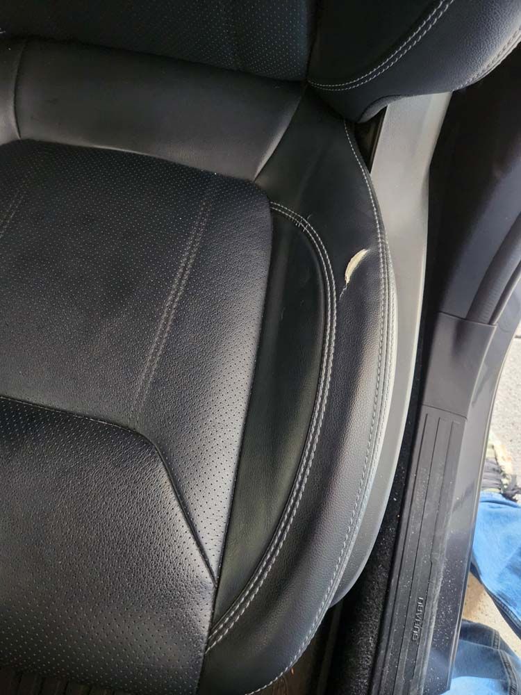 Black leather car seat with white stitching and a tear.