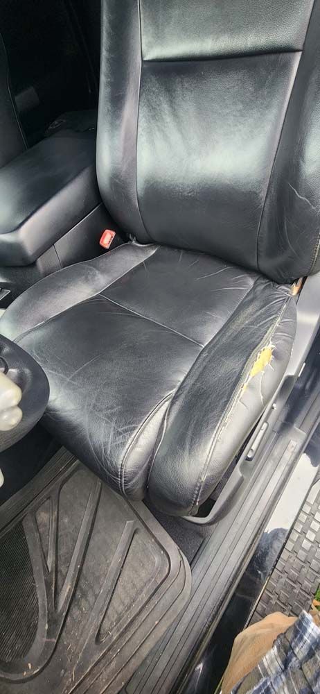 Black leather car seat with wear and tear, including a tear on the seat cushion.