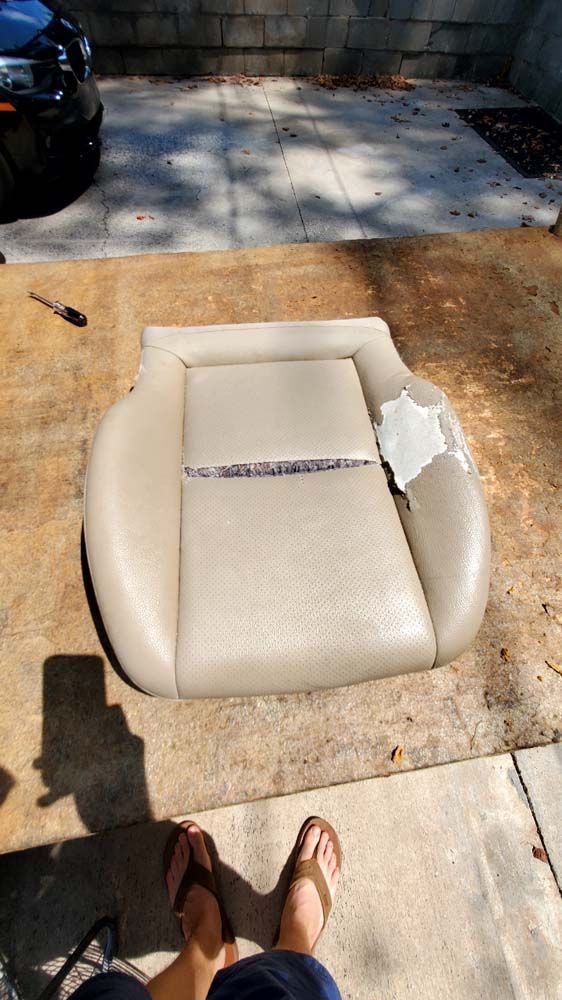 Tan car seat with torn upholstery, on a wooden surface, outside.
