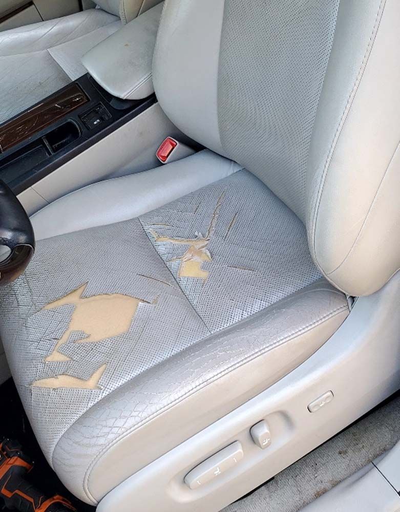 Damaged light gray car seat with flaking leather.