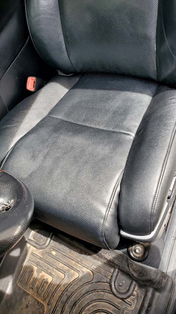 Black leather car seat with wear, showing the seat bottom and back.