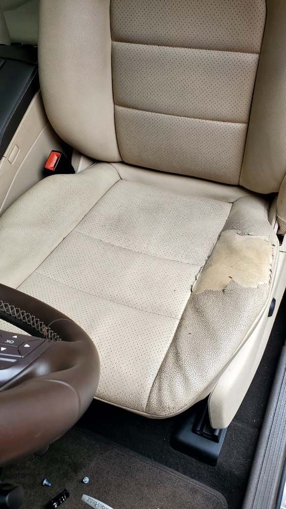 Beige leather car seat with wear and tear, including peeling on the side. Steering wheel in frame.
