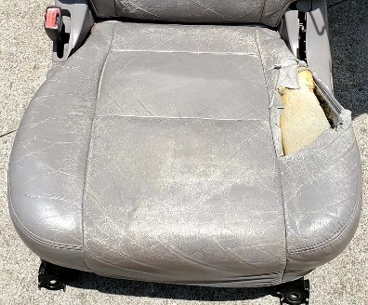 Damaged grey car seat with tears and worn surface, revealing foam padding.