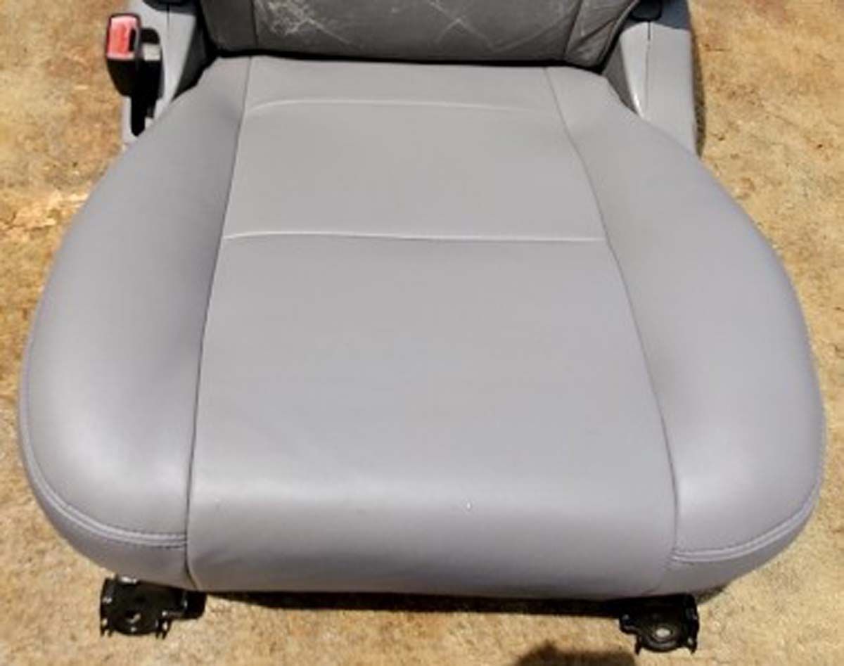 Gray leather car seat, close-up view. The seat is in good condition, with visible stitching and a seatbelt latch.