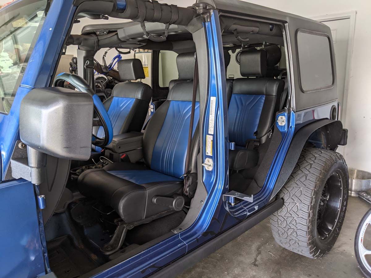 Blue Jeep Wrangler interior, doors open, black and blue seats, black hardtop.
