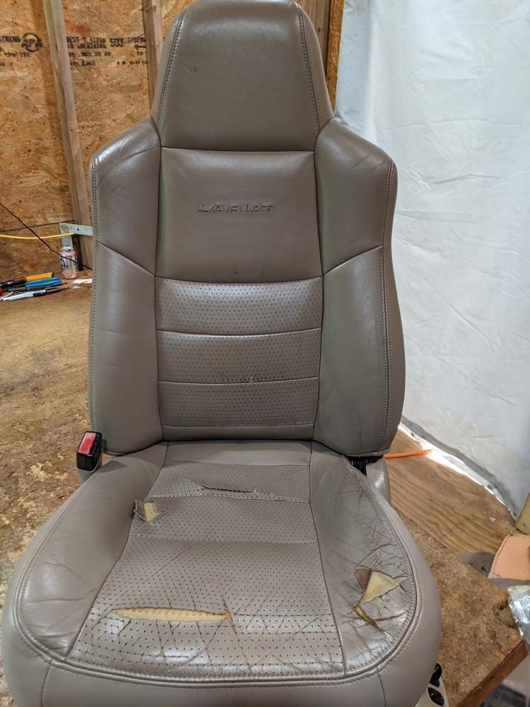 Tan car seat with damaged bottom cushion; interior setting.
