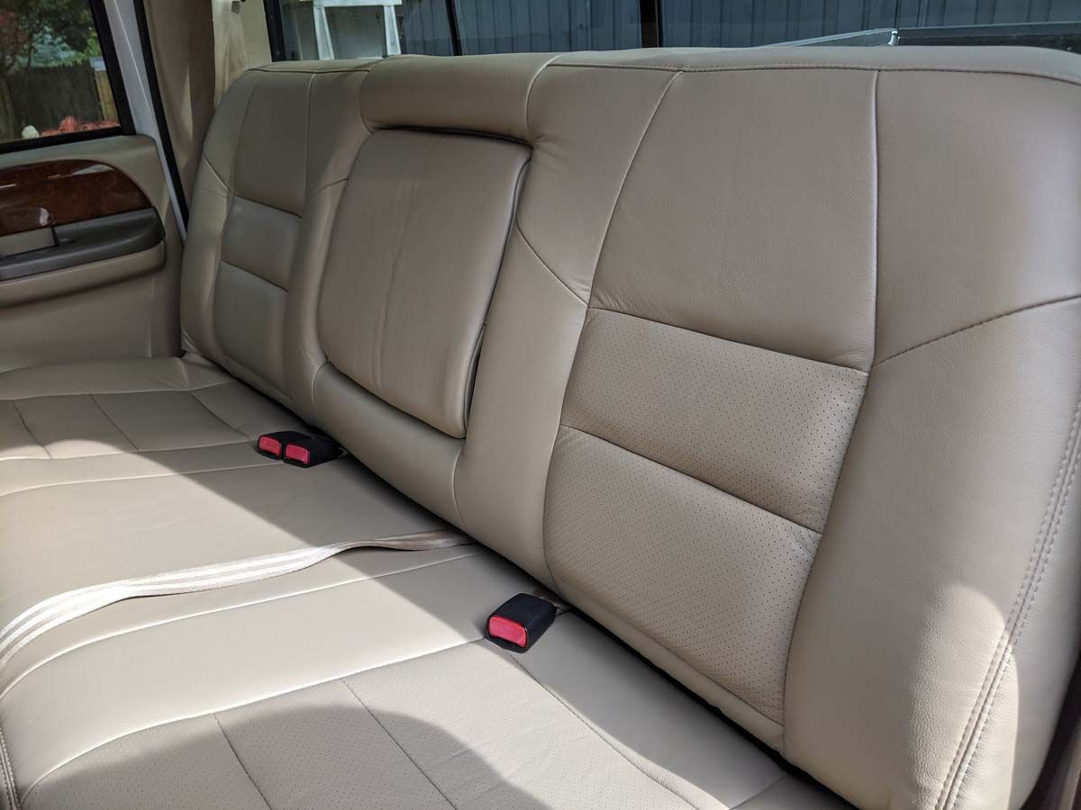 Beige leather truck backseat with two red seatbelts.