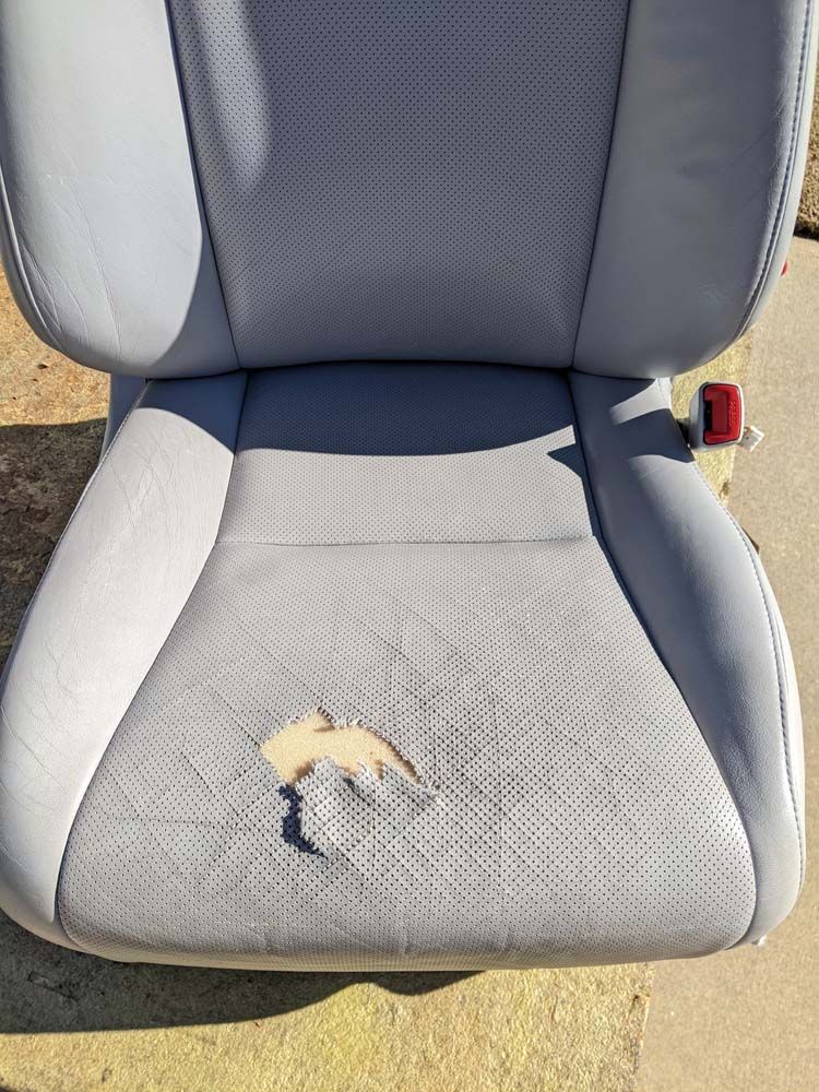 Torn gray leather car seat with a large hole in the seating area.