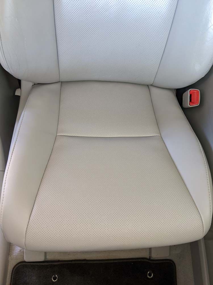 Light gray car seat with perforated leather and red seatbelt buckle.