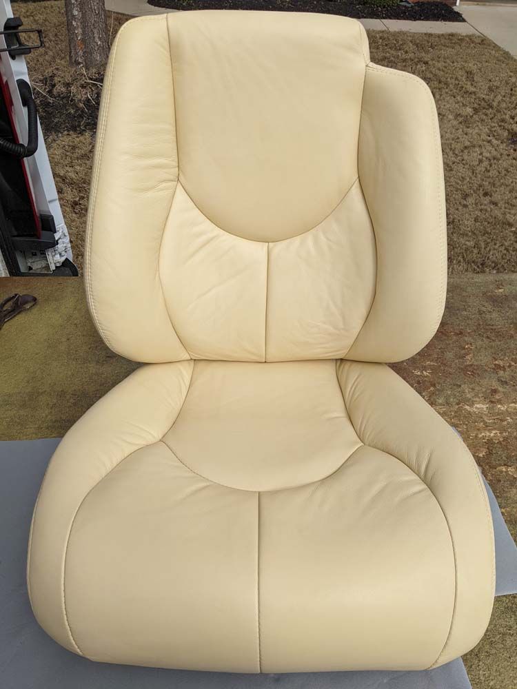 Beige car seat against a neutral background. The seat has headrest, back, and bottom cushion.