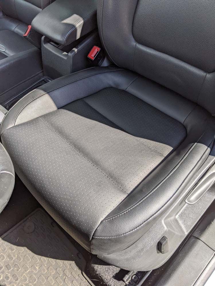 Black car seat with wear and tear, visible seam, and seat adjustment controls.