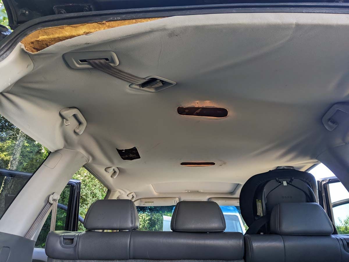 Interior of a vehicle with a sagging headliner. Gray upholstery, overhead lighting, and the back seats are visible.