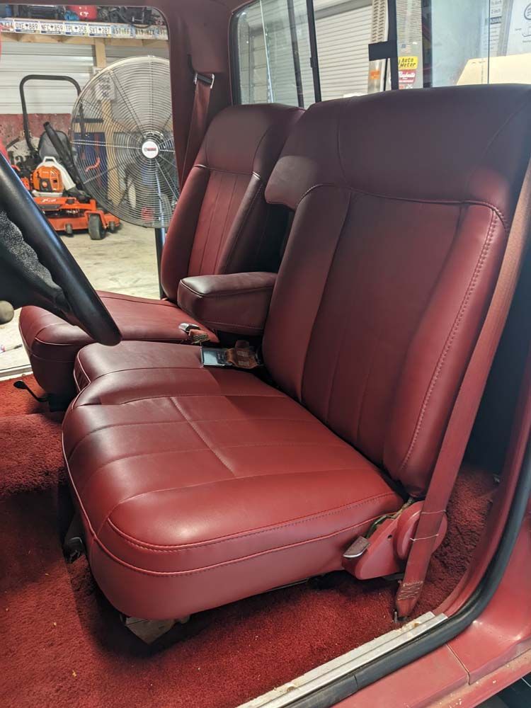 Red leather truck seats with an armrest inside a vehicle.