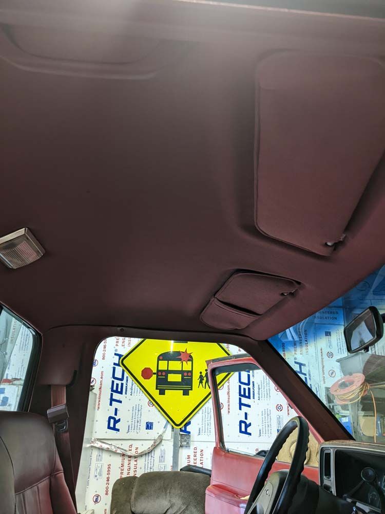 Interior of a vehicle: maroon headliner, sun visors, bus stop sign visible through the windshield.