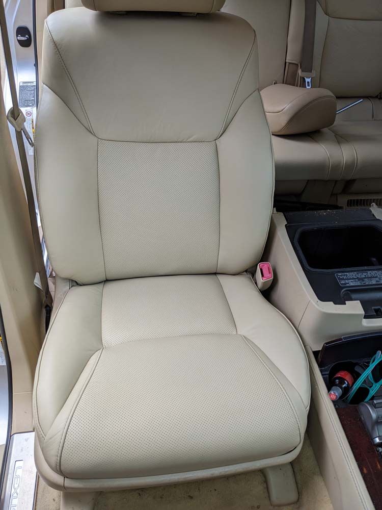 Beige leather car seat with perforated bottom, next to a center console.