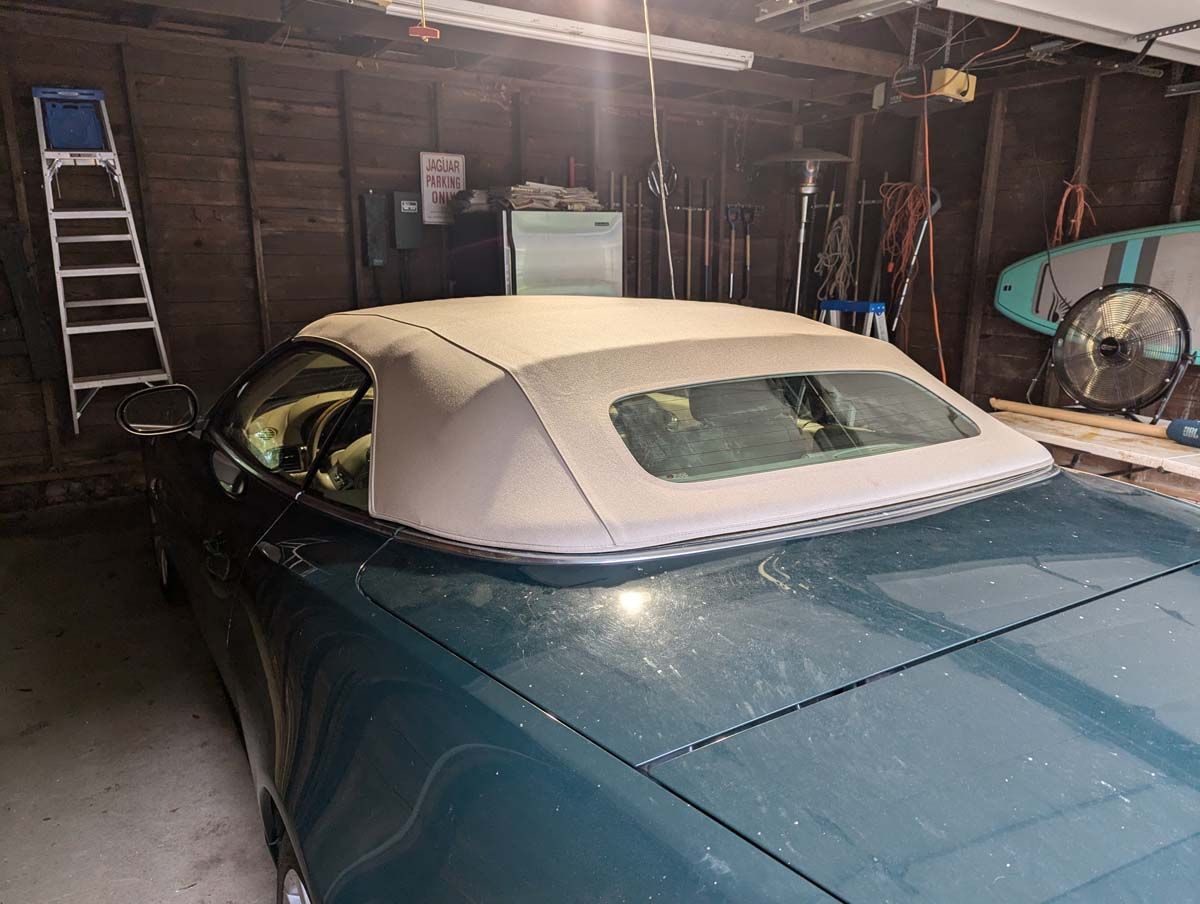 Green convertible car with beige soft top parked inside a garage.