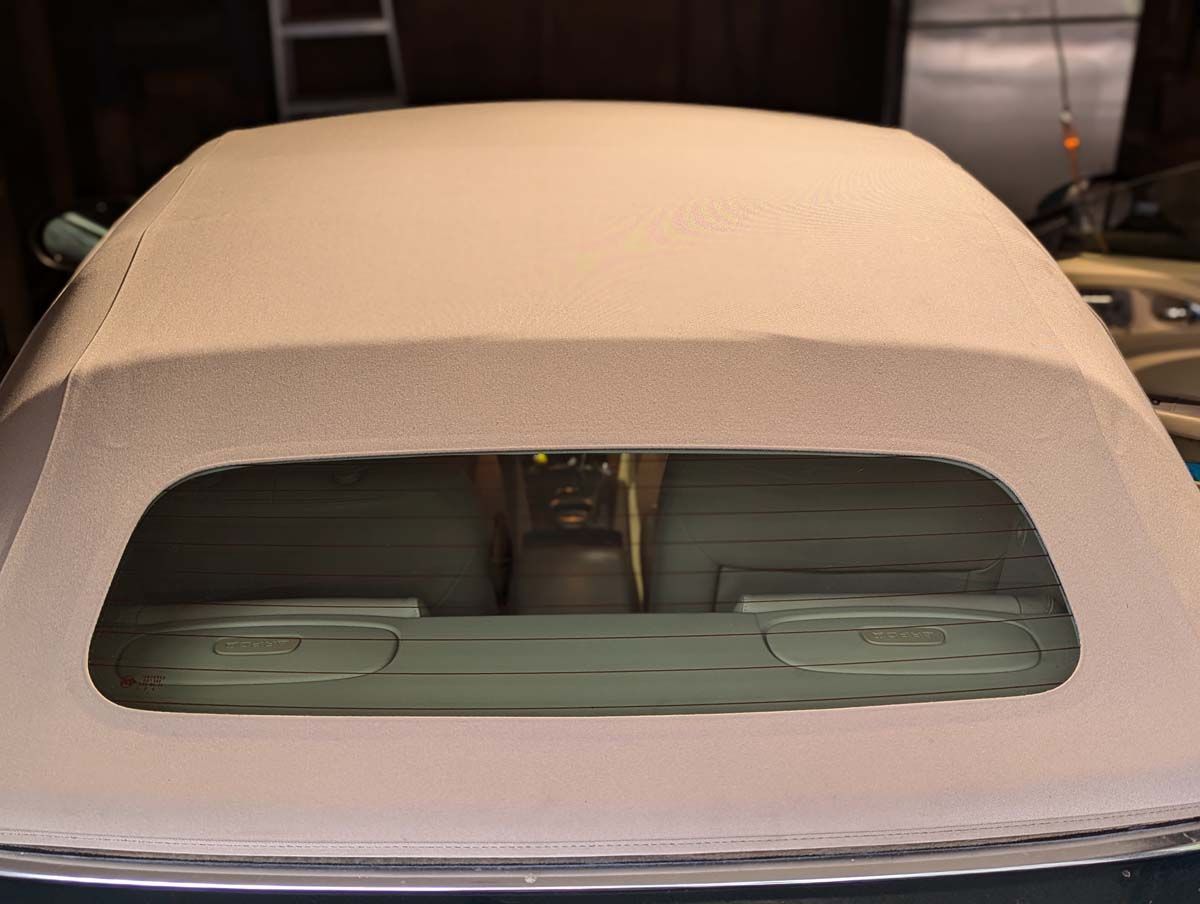 Tan convertible top with rear window open, showing car's interior.