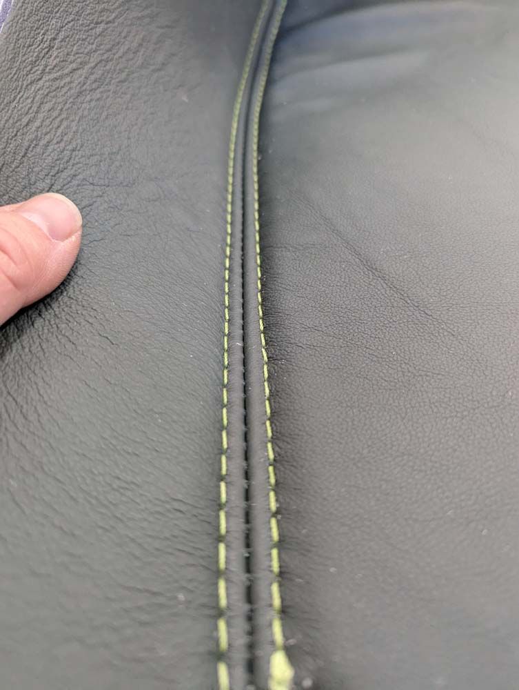 Hand holding up a dark gray, stitched seam. The stitching is green, visible on the seam.