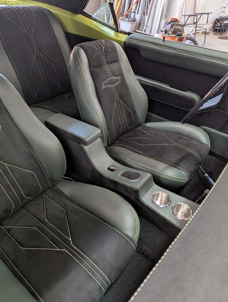 Custom car interior with green and black seats, center console, and cup holders.