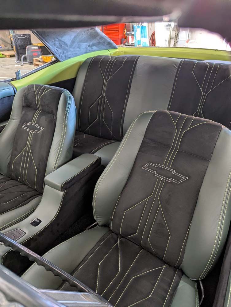 Custom car interior, gray and black seats with decorative stitching, armrest, and steering wheel.