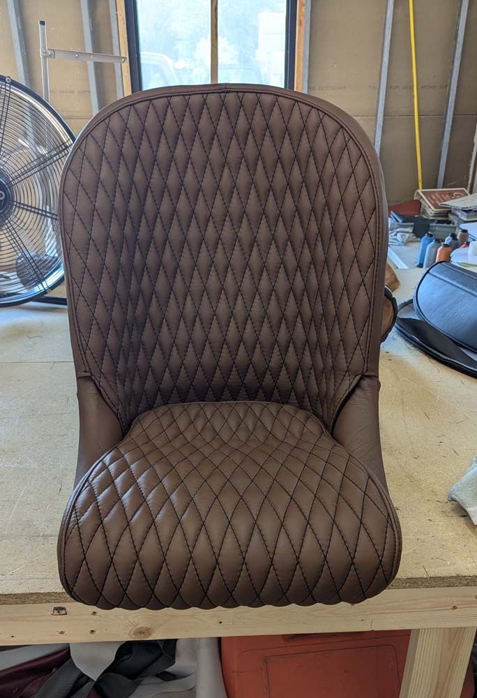 Brown leather motorcycle seat with diamond stitching, set on a wooden table.