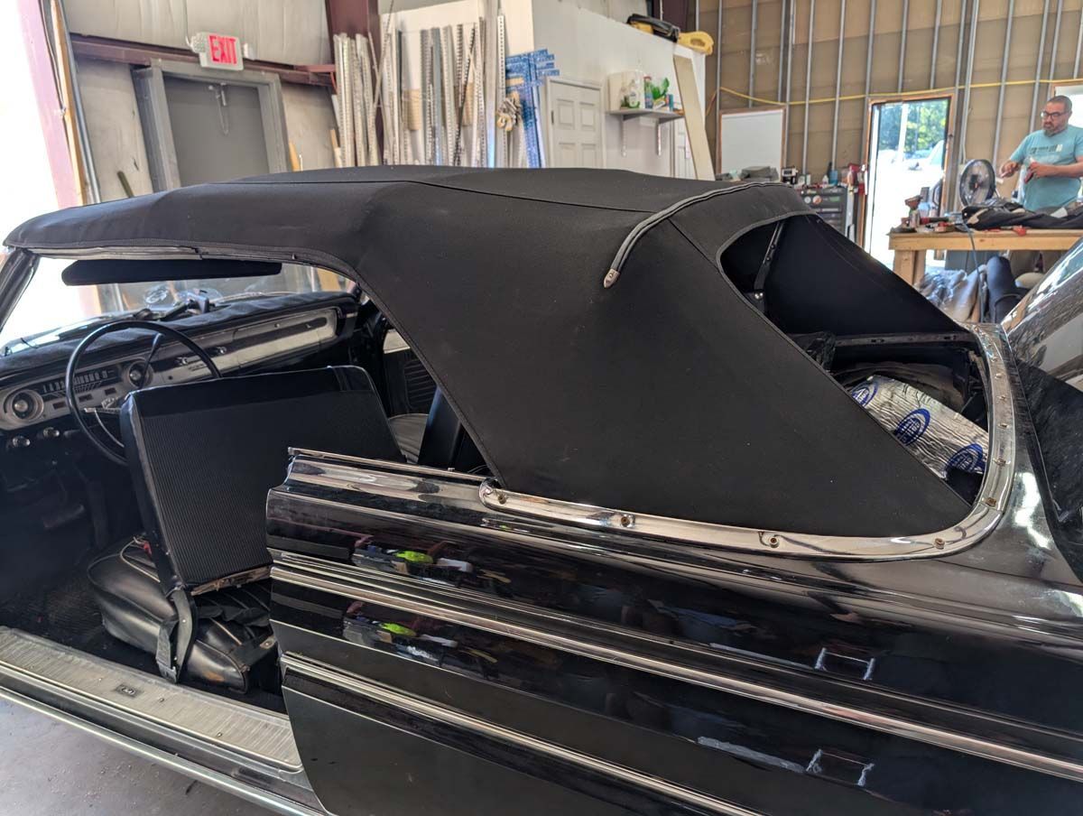 Black convertible car with new black soft top, inside a garage.