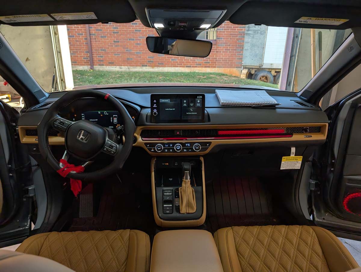 Car interior: Dashboard with tan, black, and red accents, central display screen, steering wheel, and tan seats.