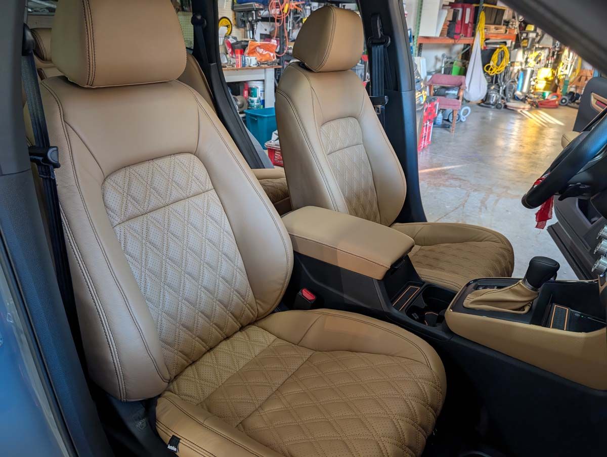 Tan leather car seats with diamond stitching in a garage setting.