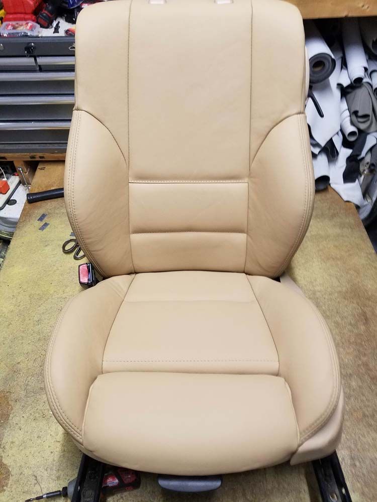 Tan leather car seat, viewed from front, sitting on a workbench.