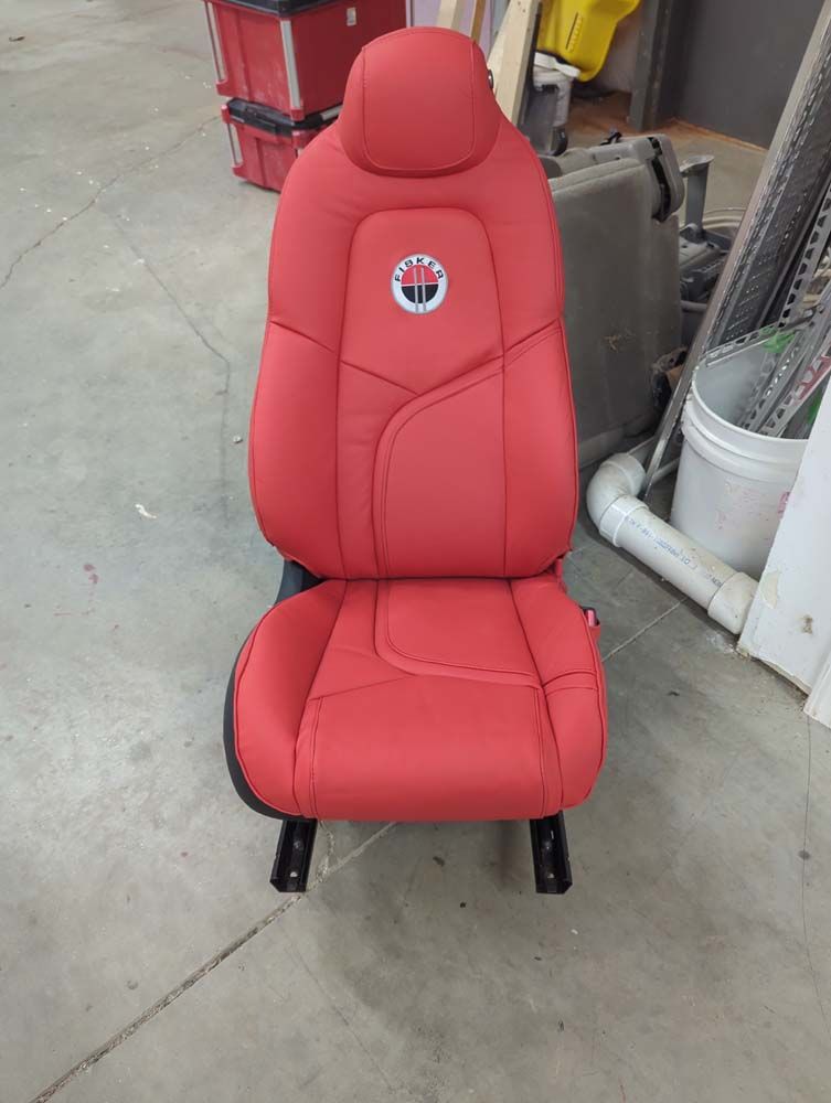 Red car seat with a logo, black legs, on a concrete floor.