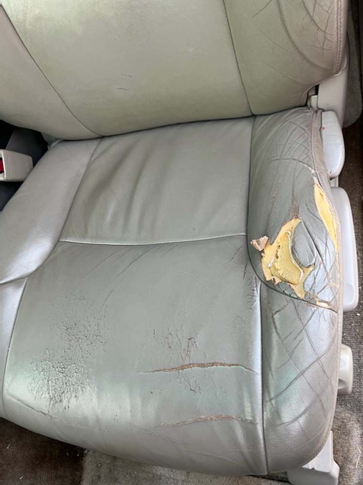 Damaged gray car seat, peeling and cracked leather.