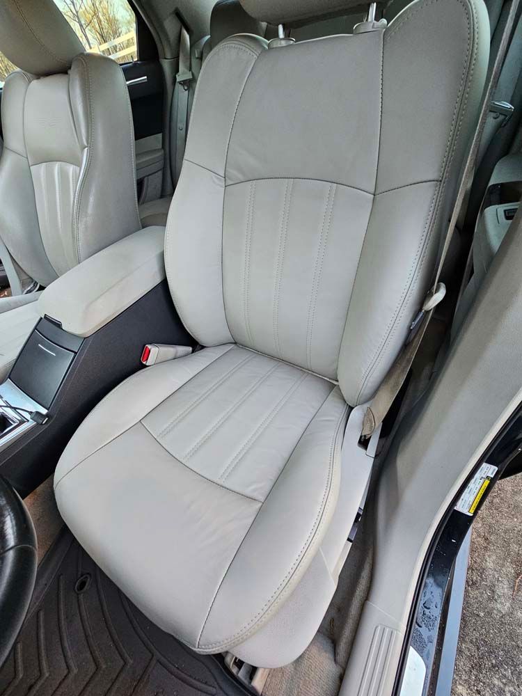 Beige leather car seat with center console and black floor mat.