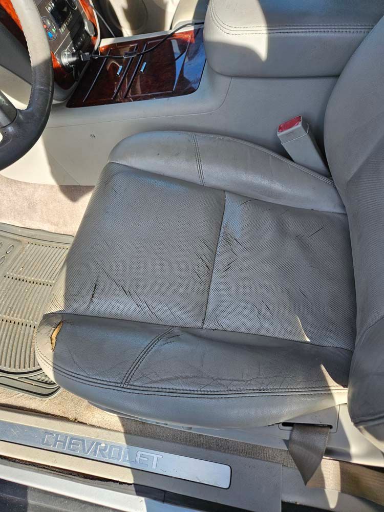 Close-up of a worn, light grey leather car seat with cracks and wear. The Chevy logo is visible on the step.