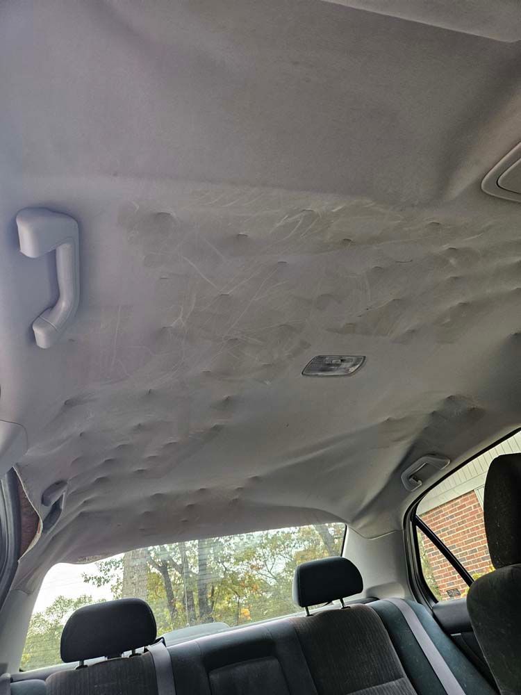 Sagging, gray fabric headliner inside a car. Includes handles, rear seats, and a dome light.