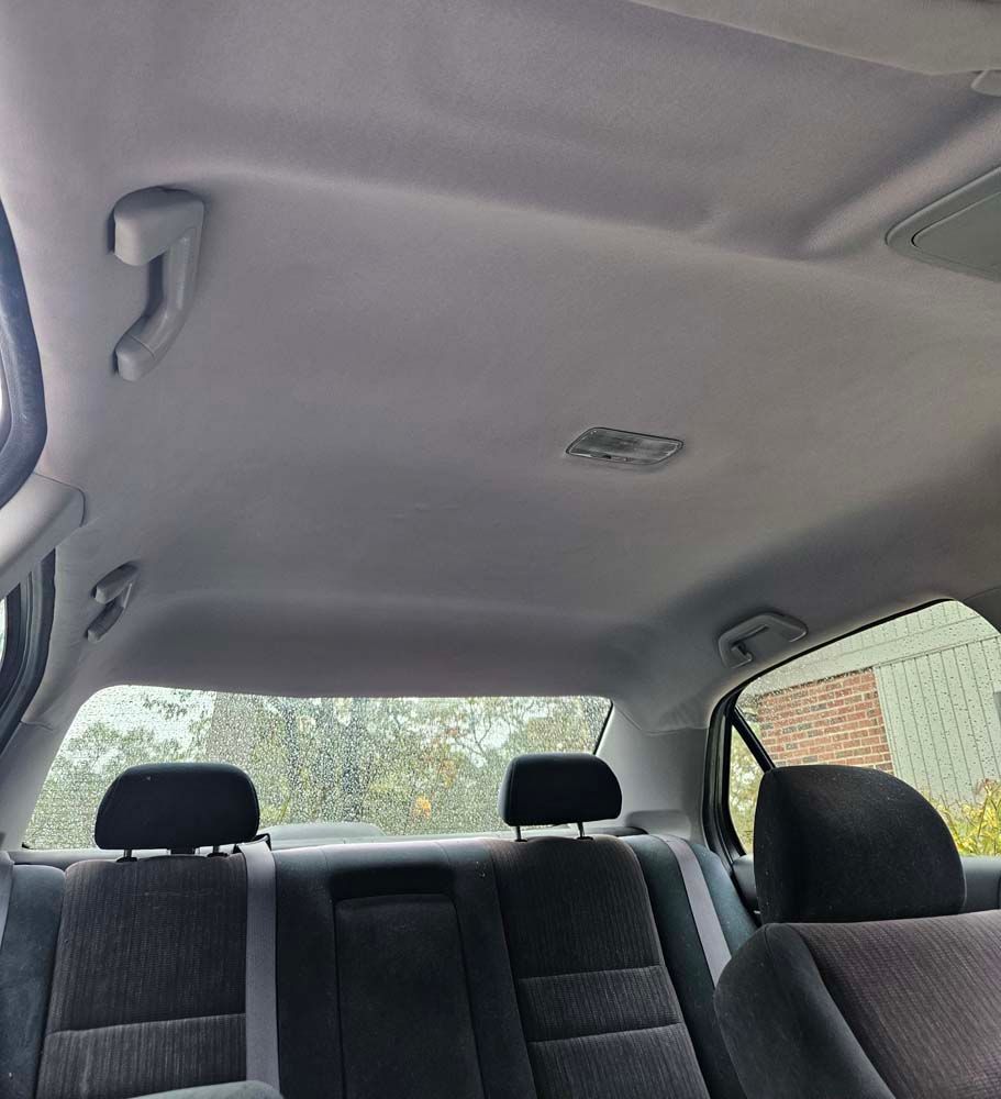 Interior view of a car's back seat. Gray headliner, seats, and a view through the rear window.