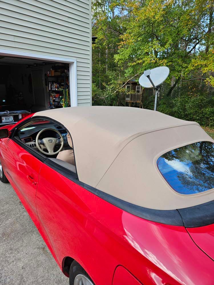 Red convertible car with tan top parked in front of a garage.